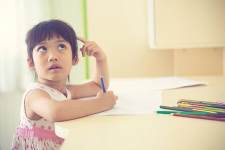 Little Asian child using a pencil to write on notebook at the deskの写真素材