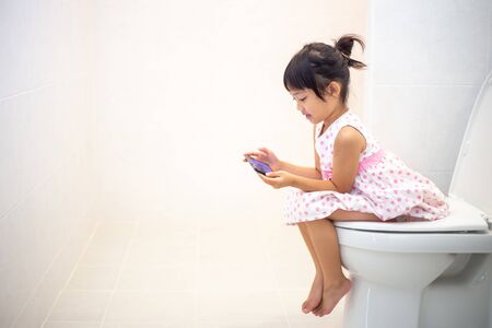 asian children sitting on a toilet and holding smartphone.の写真素材