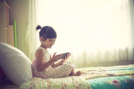 child, technology and internet concept - little girl lying in bed with smartphone at homeの写真素材