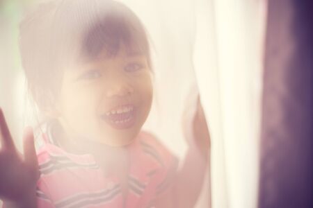 The little girl looks out because of curtainsの写真素材