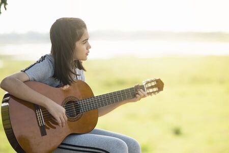 Lovely girl,playing guitar, singing ,music or happiness concept, sunset warm light tone effect.