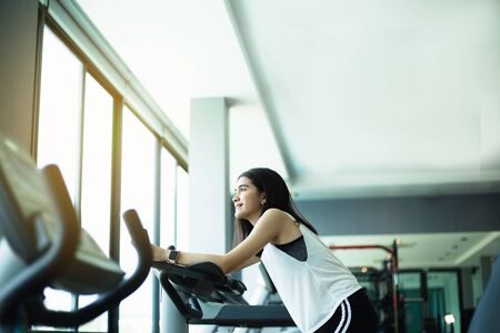 Fit young girl using exercise bike at the gym. Fitness female using air bike at gym.の写真素材