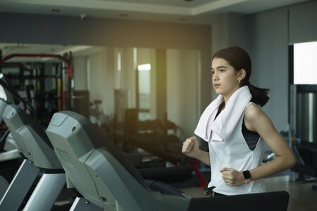 Side view of beautiful girl running on treadmill at gymの写真素材
