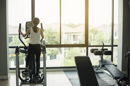 Asian girl Exercise Elliptical cardio running workout at fitness gym taking weight loss with machine...