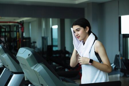 Side view of beautiful girl running on treadmill at gym
