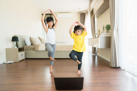 two little girls practicing yoga, stretching, fitness by video on notebook.の写真素材