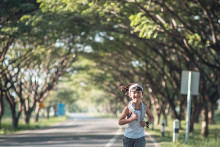 happy child girl running in the park in summer in nature. warm sunlight flare. asian little is running in a park. outdoor sports and fitness, exercise and competition learning for kid development.の写真素材