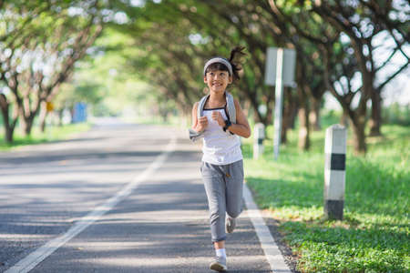 happy child girl running in the park in summer in nature. warm sunlight flare. asian little is running in a park. outdoor sports and fitness, exercise and competition learning for kid development.の写真素材