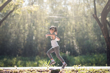 happy child girl running in the park in summer in nature. warm sunlight flare. asian little is running in a park. outdoor sports and fitness, exercise and competition learning for kid development.の写真素材