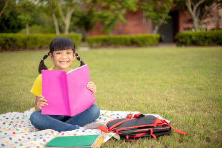 Cute Little Girl Reading Book Outside on Grassの写真素材