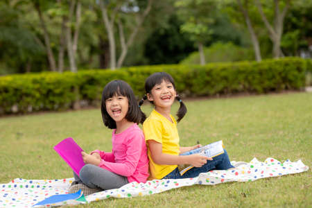two beautiful little girls reading books in the garden , sitting on grass. The concept of education and friendship.の写真素材