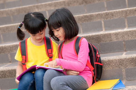 Two Little Girl reading a book together. Adorable Asian kids enjoying studying outdoors togther....