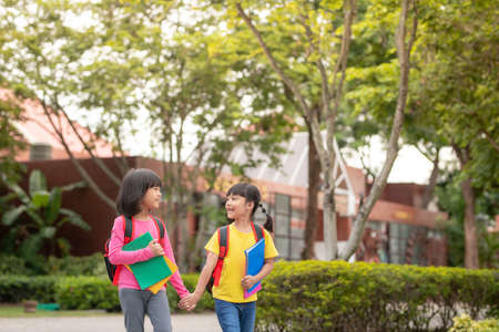 Back to school. Two cute asian child girls with school bag holding book and walk together in the...