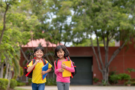 Back to school. Two cute asian child girls with school bag holding book and walk together in the schoolの写真素材