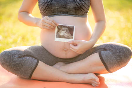Pregnant woman holding ultrasound photo near her pregnant bellyの写真素材