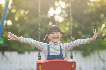 Happy little Asian girl playing swing outdoor in the parkの写真素材