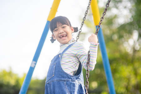 Happy little Asian girl playing swing outdoor in the parkの写真素材