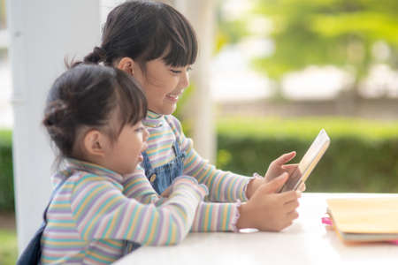 Two Asian little sisters playing with a digital tablet at home