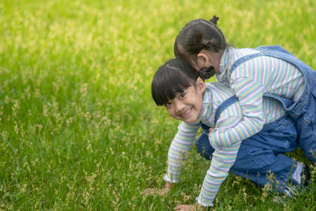Asian Little girl with elder sister at a park riding on her backの写真素材