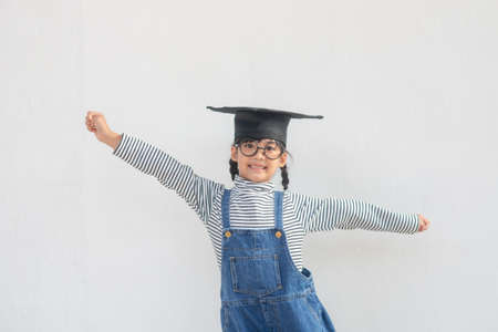 children girl wearing a graduate cap over white background very happy and excited doing winner gesture with arms raised, smiling and screaming for success. Celebration concept.の写真素材