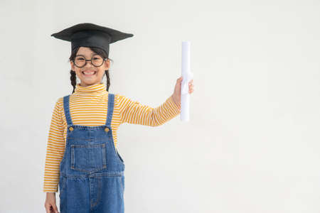 Asian Little girl wearing a graduation cap and holding diploma on white backgroundの写真素材