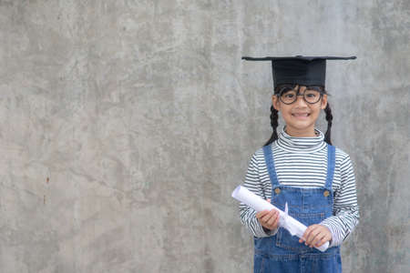 Happy Asian school kid graduate in graduation capの写真素材