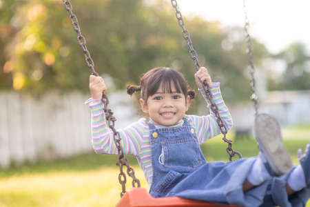 Happy little Asian girl playing swing outdoor in the parkの写真素材