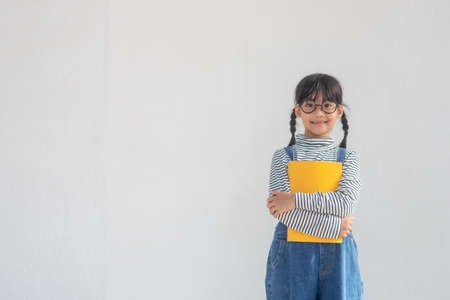 Back to school. A funny little girl in glasses on white background. Child from elementary school with a book. Educationの写真素材