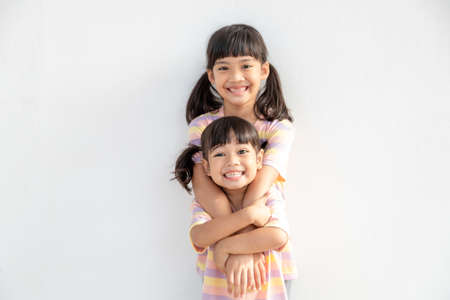 Cute happy Asian siblings hugging cuddling feeling love and connection, smiling kid girl sister...