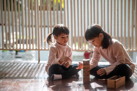 two Asian girls playing wooden stacks at homeの写真素材