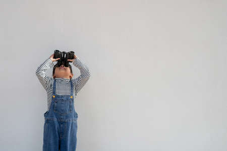 Little Asian girl looking through binoculars in white background. Explore and adventure concept.の写真素材