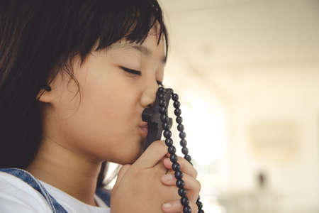 Little Asian girl praying with holding the cross, Christian concept.の写真素材
