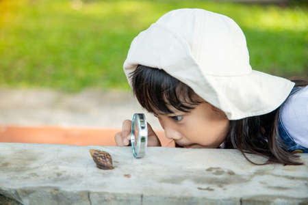 Happy kid girl exploring nature with a magnifying glass and a snail. He having fun in the garden....