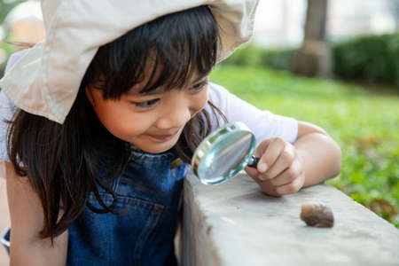 Happy kid girl exploring nature with a magnifying glass and a snail. He having fun in the garden. The concept of the kid is ready to go to school.の写真素材