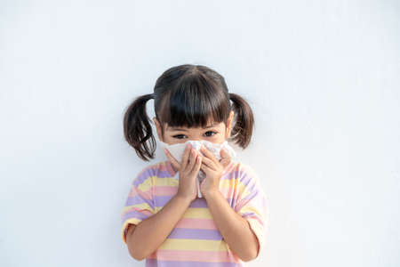Asian child girl sick with sneezing on the nose and cold cough on tissue paper because weak or virus and bacteria from dust weather and kindergarten and preschoolの写真素材