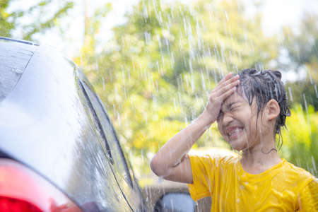 Happy Asian girl washing car on water splashing and sunlight at homeの写真素材