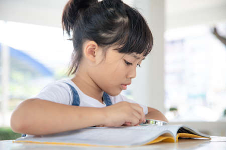 Asian Little girl reading the books on the desk with a magnifying glassの写真素材