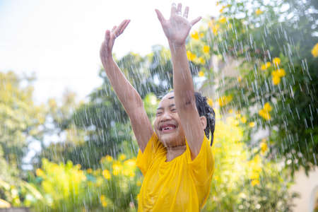 Happy Asian little child girl having fun to play with the rain in the sunlightの写真素材