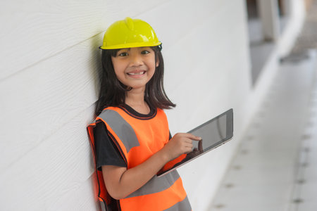 Portrait Asian kid girl wearing a reflective shirt and hard hat safety writing record on tablet. To learning and enhance development, little architect.の写真素材