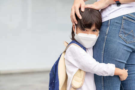 mother accompanies the child to school. mom supports and motivates the student. the little girl wearing a face mask does not want to leave her mother. fears primary school.の写真素材