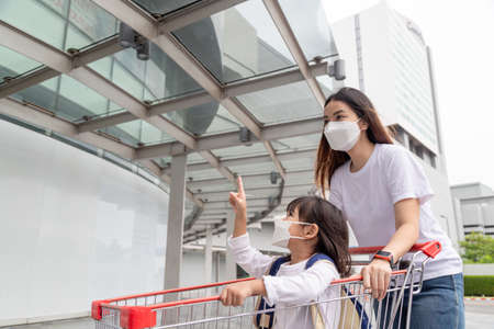 Shopping with kids during a virus outbreak. Asian Mother and daughter wearing surgical face mask going to the supermarket.の写真素材
