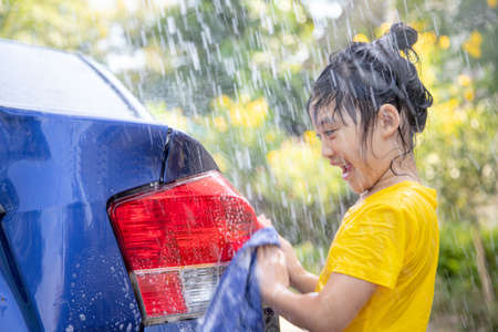 Happy Asian girl washing car on water splashing and sunlight at homeの写真素材