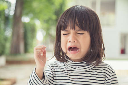 Portrait of Asian crying little girl with little rolling tears weeping emotion, hurt in pain fit drops cheek. Young crying panic drama Asian toddler.の写真素材