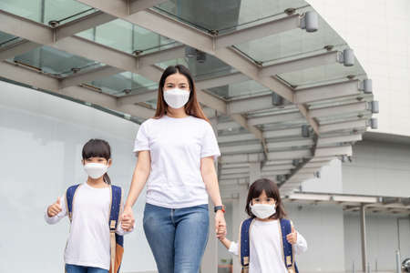 Asian mother helps her daughter wearing a medical mask for protection Covid-19 or coronavirus outbreak prepare to go to school when back to school order.の写真素材