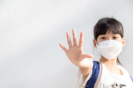 Back to school.Little Asian girl wearing a mask for protection. show stop hands gesture to stop coronavirus outbreak.の写真素材