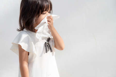 Asian child girl sick with sneezing on the nose and cold cough on tissue paper because weak or virus and bacteria from dust weather and kindergarten and preschoolの写真素材