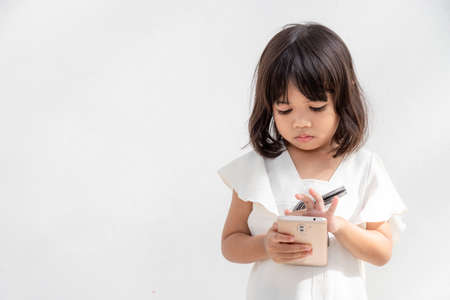 A little girl is concentrated on the phone, look at the smartphone, technology concept for children, profile view, isolated on white background, copy spaceの写真素材