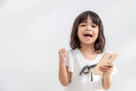 Excited Asian little girl is using a smartphone, empty space shot isolated on white backgroundの写真素材