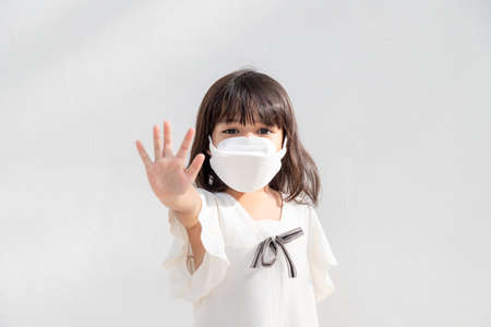 Back to school.Little Asian girl wearing a mask for protection. show stop hands gesture to stop coronavirus outbreak.の写真素材