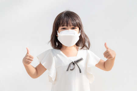 Little asian girl wearing mask for protect pm2.5 and show thumbs up gesture for good air outdoor.Air pollution pm2.5 and Coronavirus conceptの写真素材